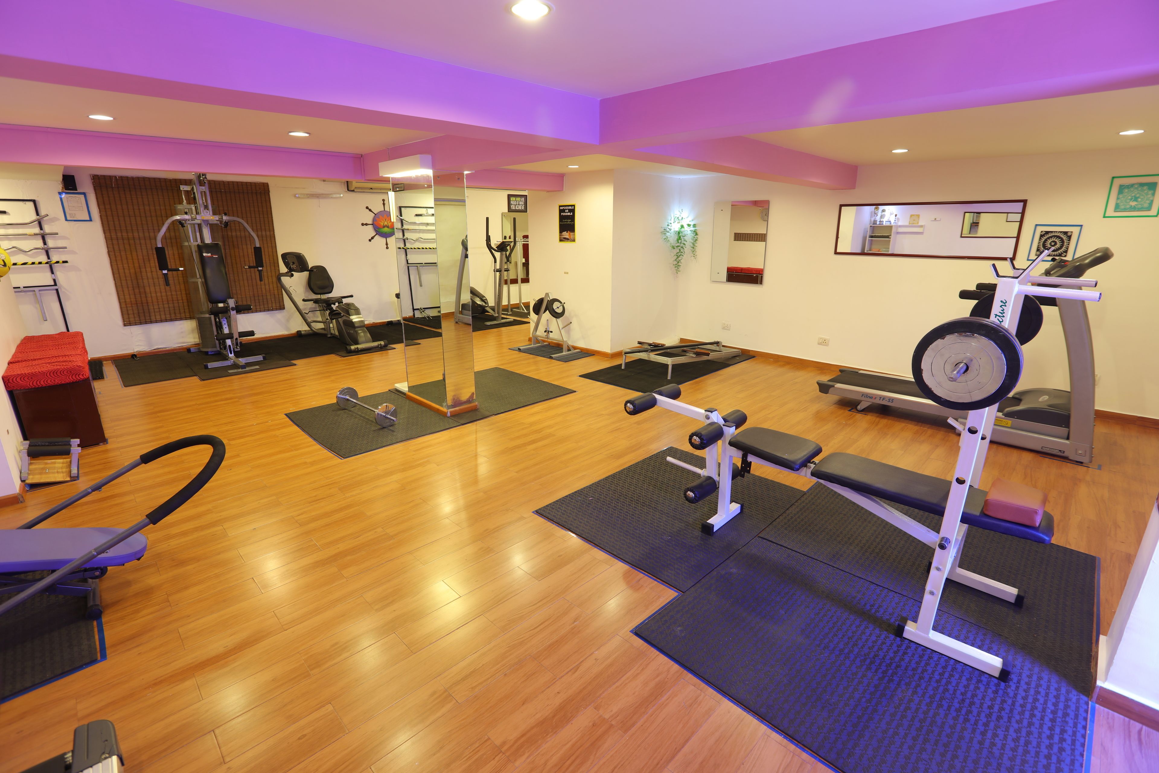 Un gimnasio con diversos equipos de ejercicio, suelo de madera y colchonetas.