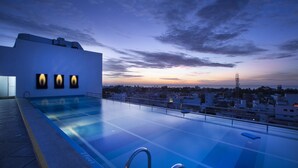Una piscina en la azotea con vista a la ciudad al anochecer.