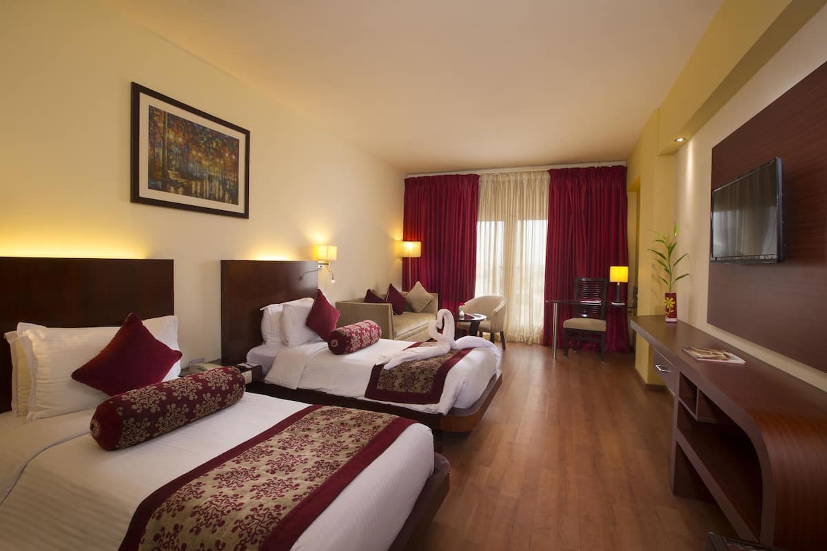 A hotel room with two beds, a desk, a chair, and a TV.