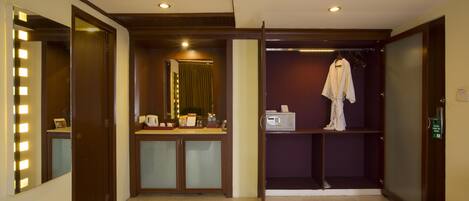 Habitación de hotel con tocador, una bata colgada en un perchero y un espejo con luces.
