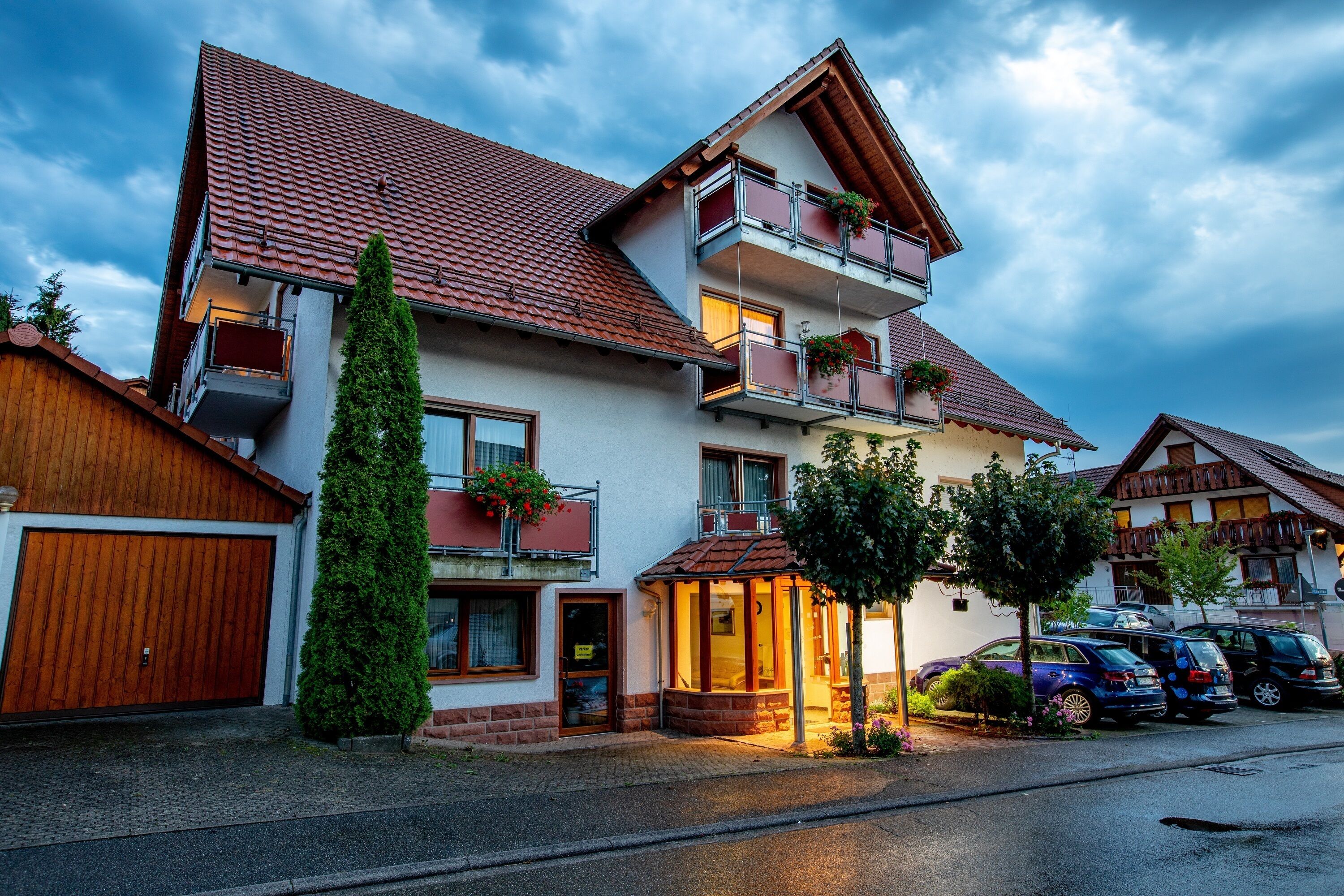 A multi-story residential building with a red-tiled roof, balconies with flower boxes, and a small porch area.