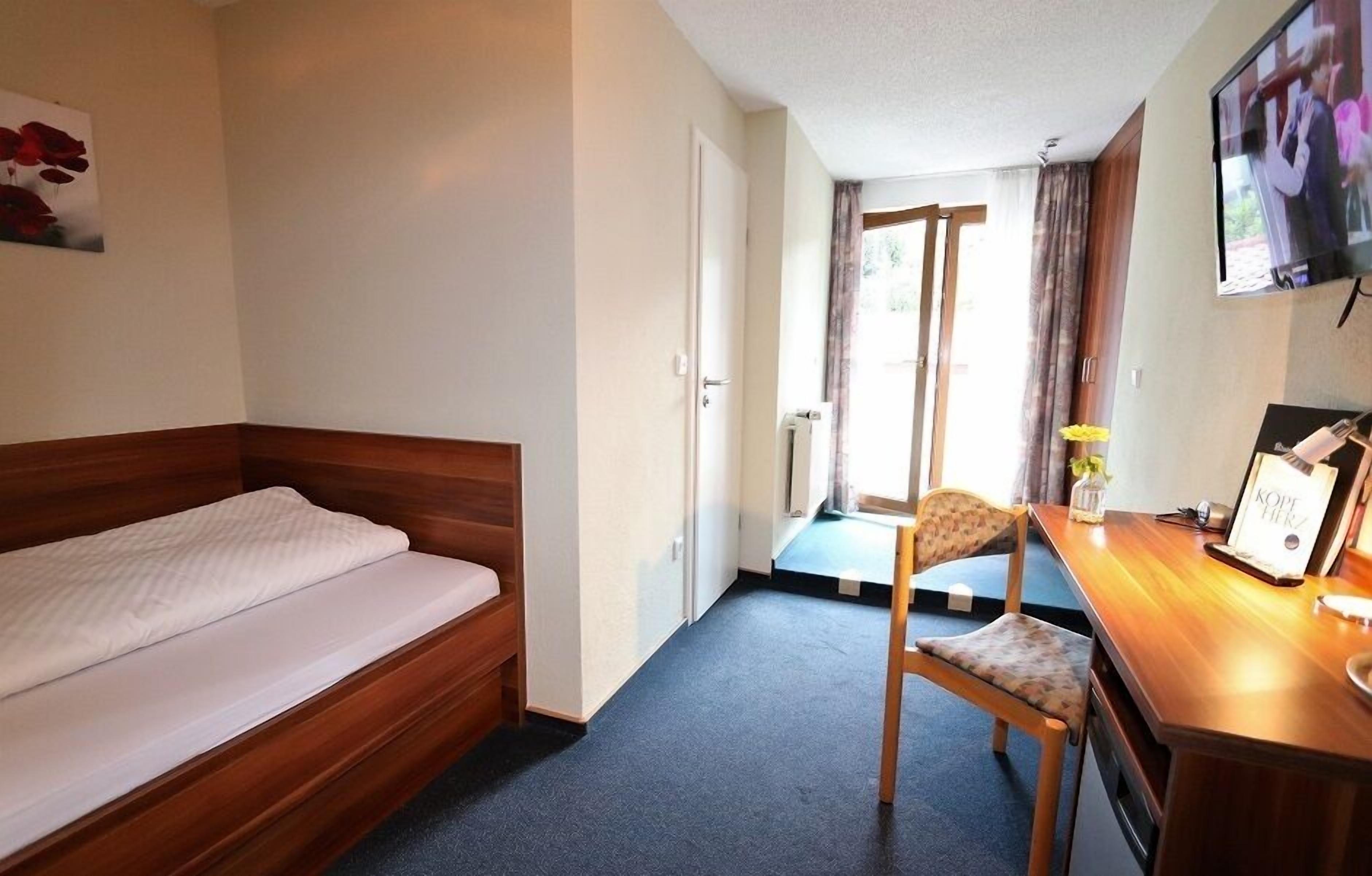 Een hotelkamer met een eenpersoonsbed, een houten bureau, een stoel, een televisie en uitzicht op de omgeving.
