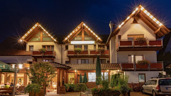 Un hotel de estilo chalete tradicional con varios balcones, mobiliario exterior y una entrada bien iluminada.