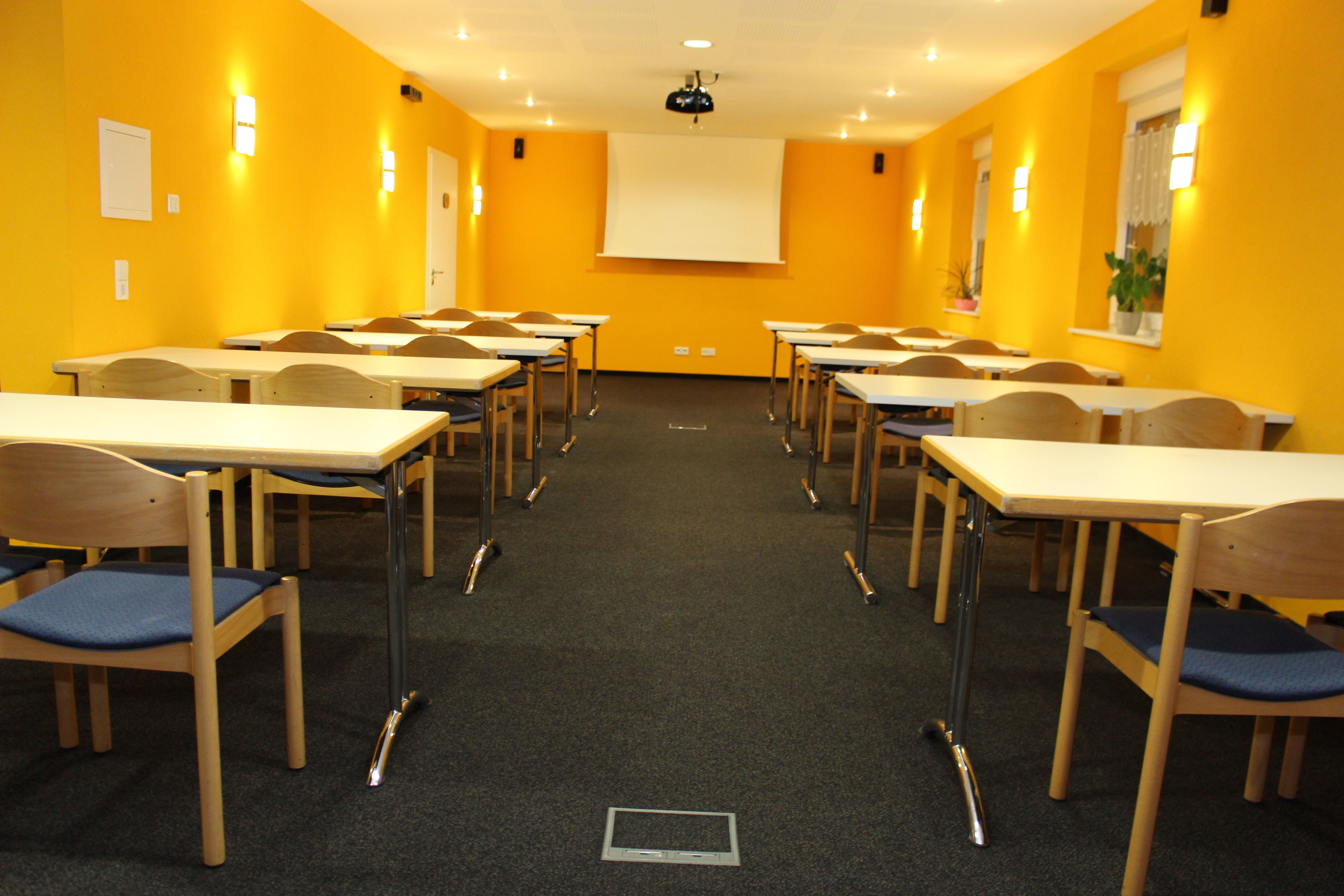 A conference room with multiple tables and chairs, a projector screen, and a carpeted floor.