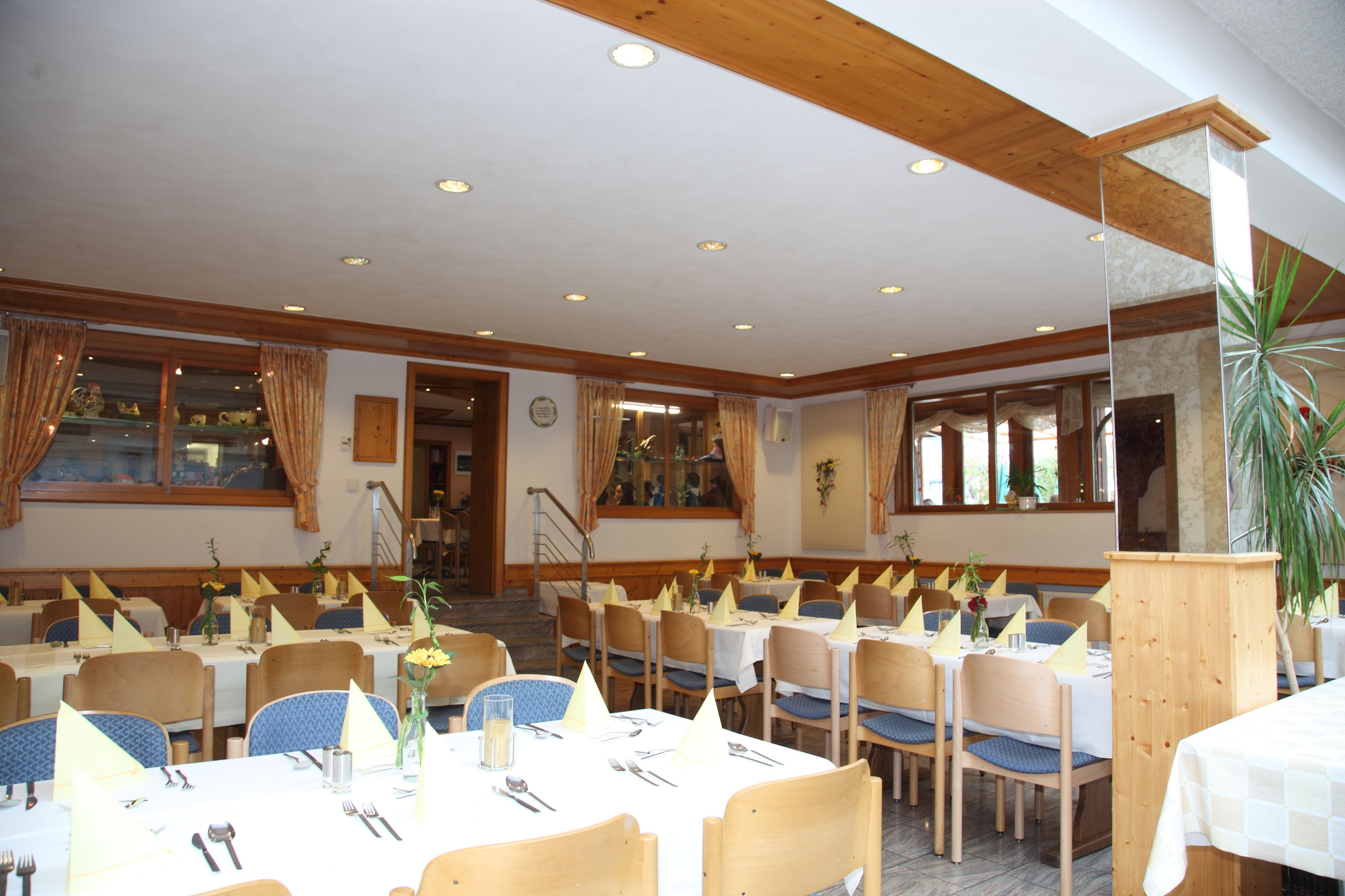 Un comedor con varias mesas dispuestas para comer, sillas de madera y una escalera que sube a un nivel superior.