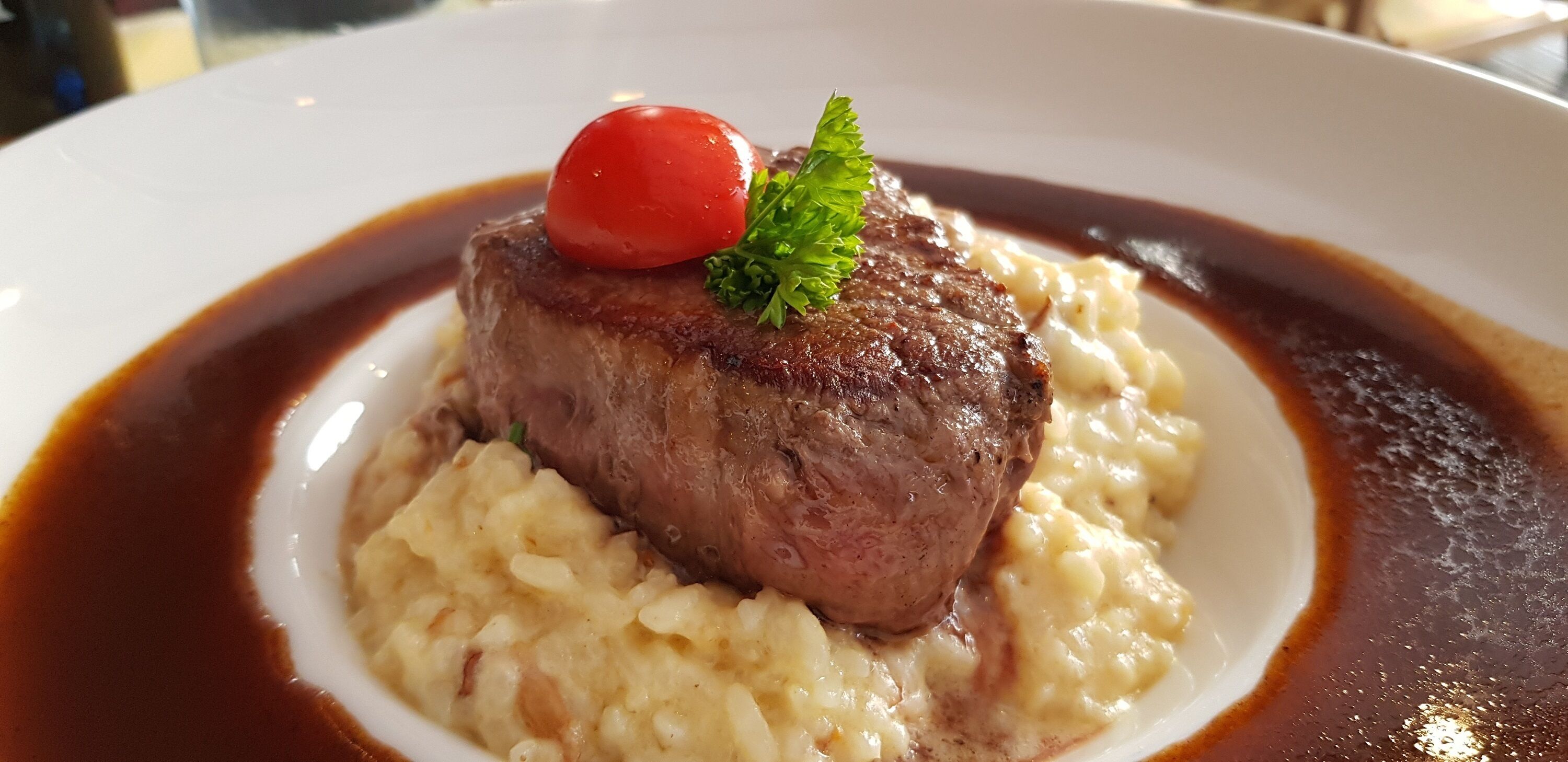 Un plato de comida con un bistec, puré de papas y un tomate cherry como adorno.