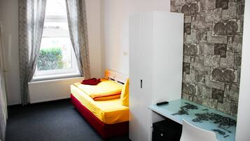 Ein Schlafzimmer mit einem Bett, einem Kleiderschrank, einem Schreibtisch und einem Fenster mit Vorhängen.
