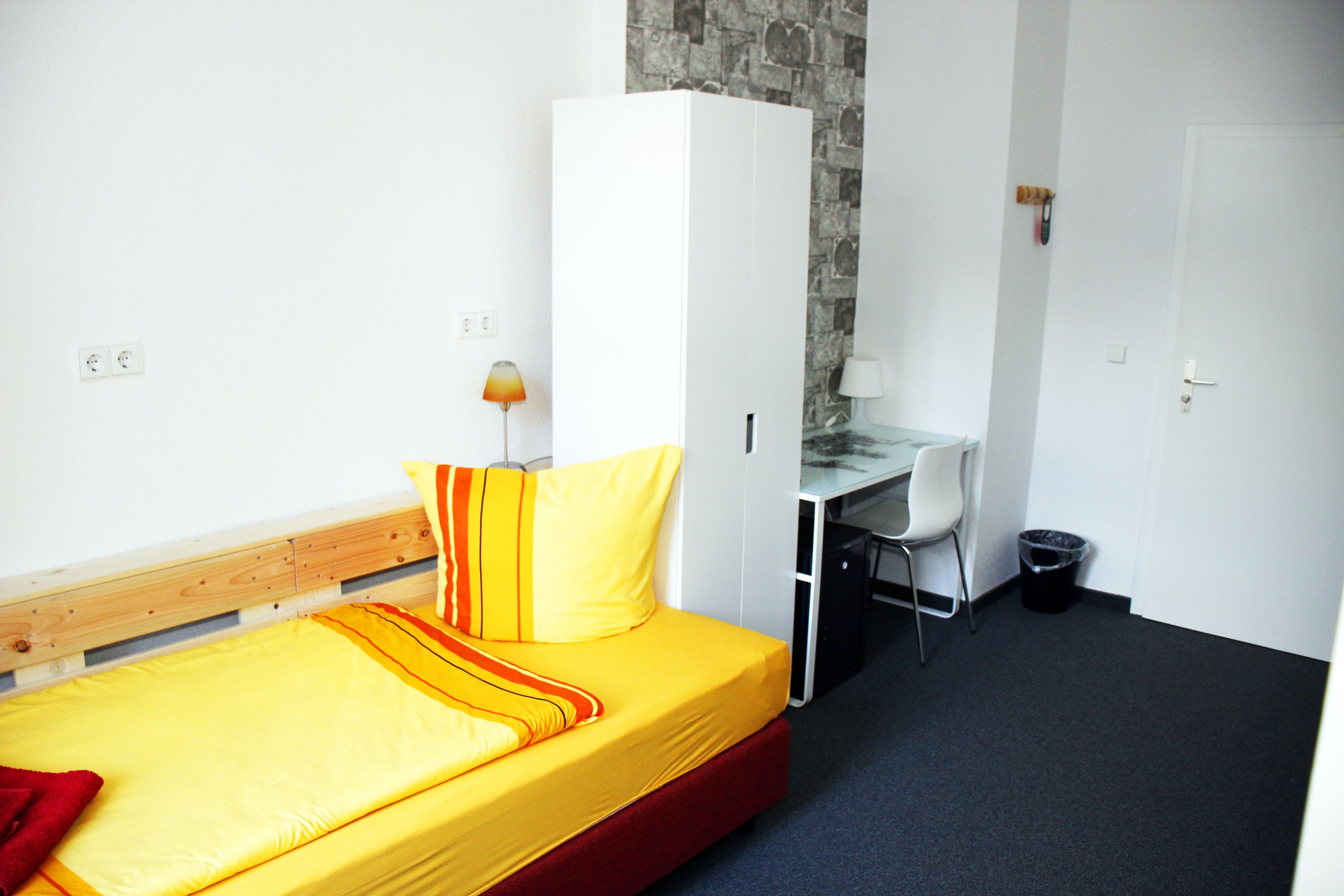 Ein kleines Zimmer mit einem Bett, einem Schreibtisch und einem Kleiderschrank.