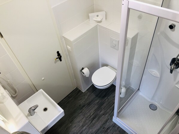 A small, compact bathroom with a toilet, sink, and a glass shower enclosure.