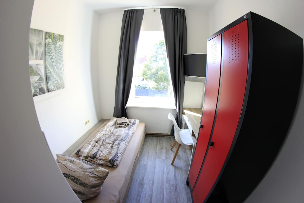 A compact room with a bed, a desk, and a wardrobe.