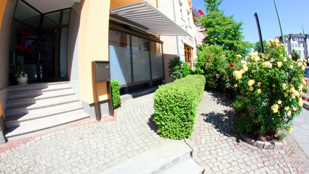 Ein Hotel mit Eingang, Glasdoor, Stufen und einem kleinen Garten mit gelben Blumen.