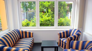 Ein Zimmer mit zwei gestreiften Sesseln und einem kleinen Tisch, ein Fenster mit Blick ins Grüne und ein Heizkörper an der Wand.