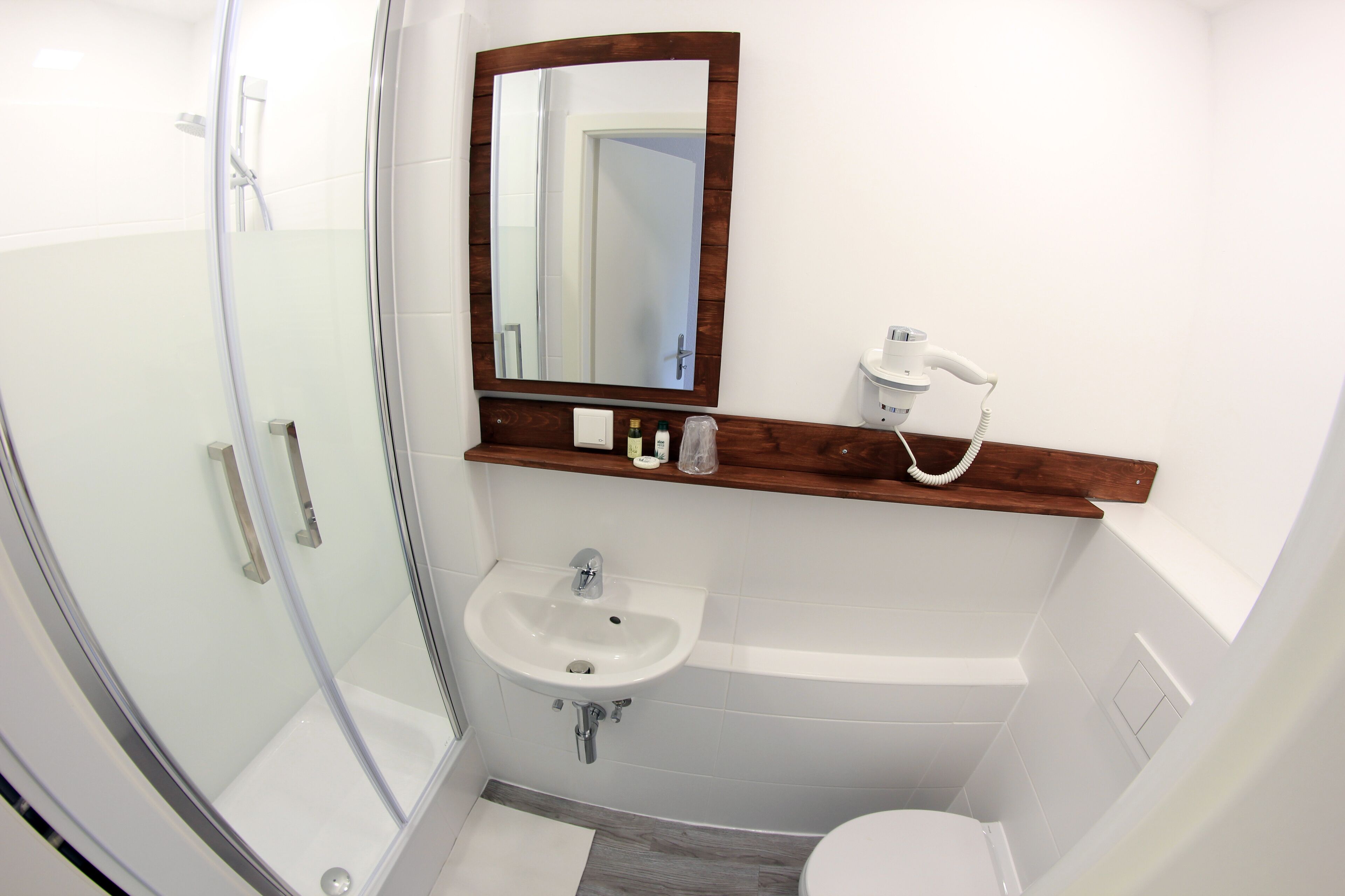 A bathroom with a glass shower enclosure, a sink, a toilet, and a mirror with a wooden frame.