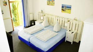 Ein Doppelbett mit blauer Matratze und weißen Kissen, ein weißer Nachttisch mit Lampe sowie ein kleiner Beistelltisch.