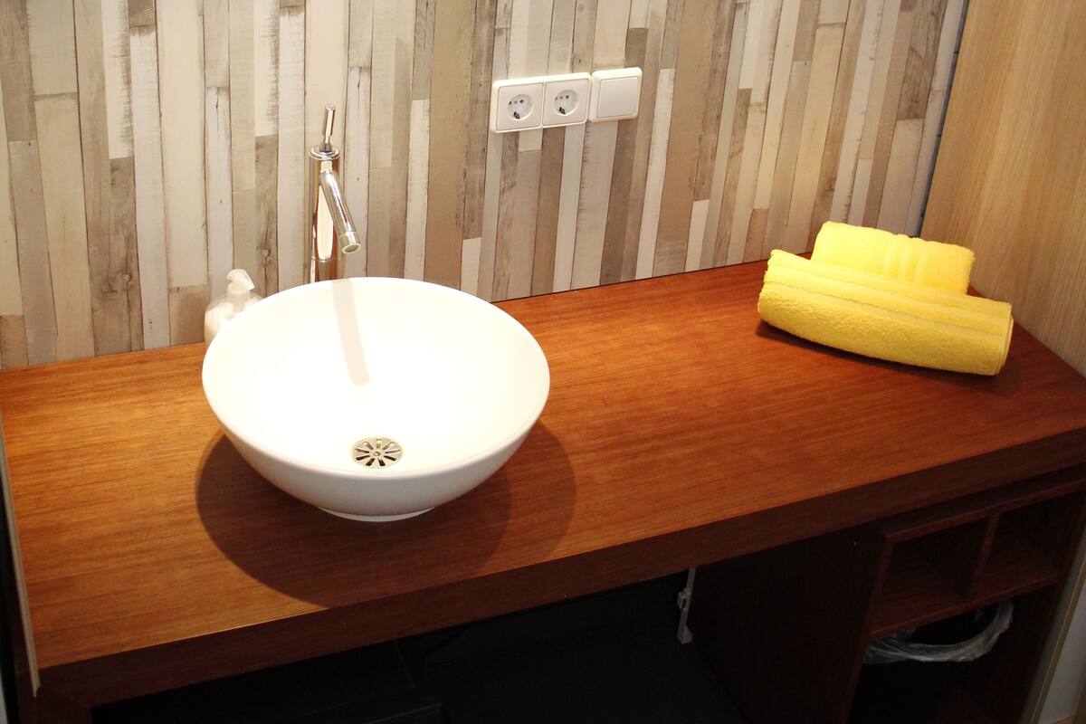 A bathroom with a wooden vanity, a white sink, a mirror, and a yellow towel.