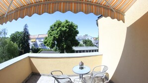 Ein Balkon mit gestreiftem Sonnensegel, zwei Metallstühlen, einem kleinen Tisch und einer Laterne.