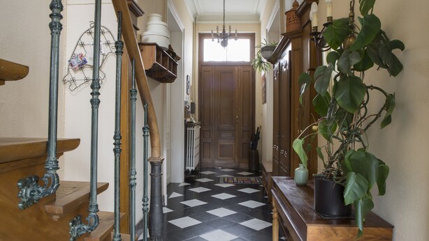 A hallway with a checkered floor, a wooden staircase, and a potted plant. - BnB Les Greniers de Madelgaire (Soignies)