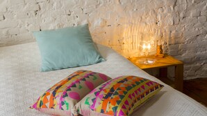 A bed with a quilted white cover, two pillows, one plain and one patterned, and a small wooden nightstand with a lamp. - BnB Les Greniers de Madelgaire (Soignies)