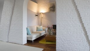 A modern living room with a white brick wall, a white sofa with light blue cushions, a glass coffee table, and a floor lamp. - BnB Les Greniers de Madelgaire (Soignies)