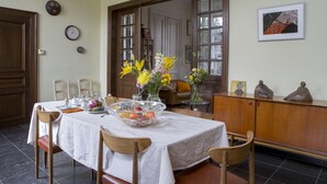 A dining area with a table set for four, surrounded by chairs, a wooden cabinet, and a bookshelf. - BnB Les Greniers de Madelgaire (Soignies)