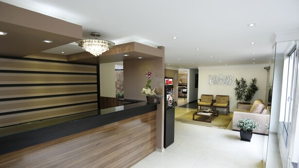 A hotel reception area with a wooden reception desk, a chandelier, and a seating area with sofas and a coffee table. - Hotel King (São José do Rio Preto)