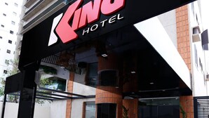 A hotel entrance with a prominent sign, outdoor seating, and a modern building facade. - Hotel King (São José do Rio Preto)