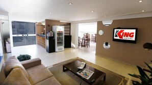 A hotel lobby with a sofa, a coffee table, a refrigerator, and a dining area in the background. - Hotel King (São José do Rio Preto)