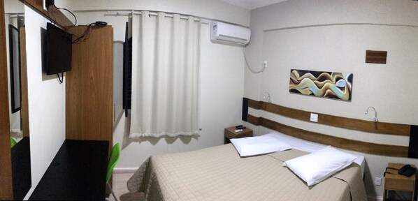 Ein Hotelzimmer mit Bett, Nachttisch, Fernseher, Klimaanlage und einem Gemälde an der Wand.
