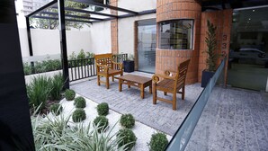 A patio with wooden furniture, a brick wall, and a glass railing. - Hotel King (São José do Rio Preto)