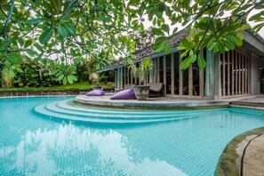 A pool with clear blue water, surrounded by lush greenery and a building with large windows. - Maya Villa-Private Pool (Seminyak)