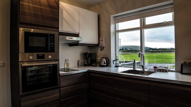 A modern kitchen with built-in appliances, a large window with a view of a green landscape, and a sink. - Breidamyri Farm Apartments (Laugar)
