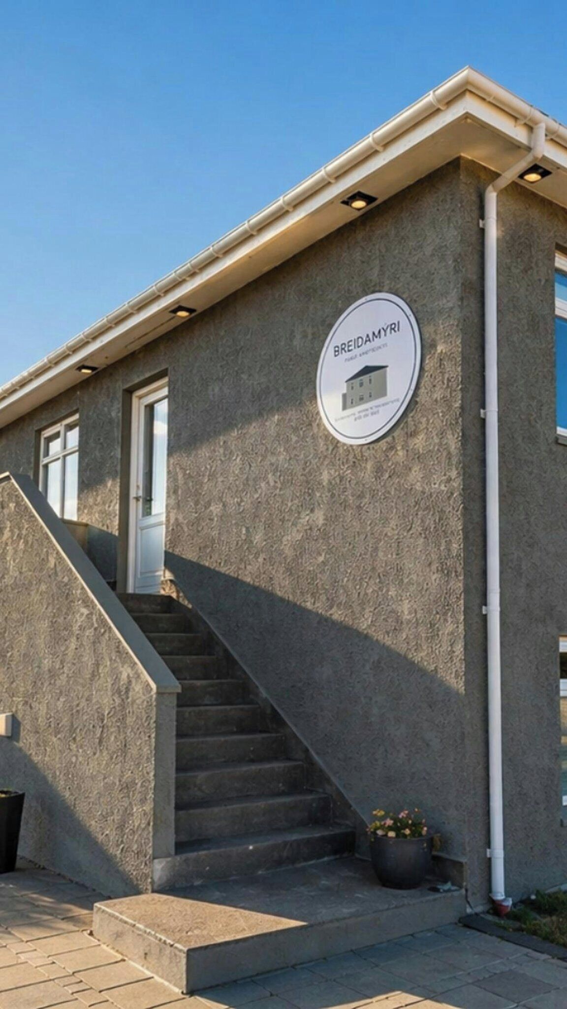 A building with a sign reading 'BREIDAMYRI' and a staircase leading to the entrance.