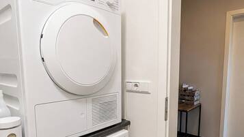 A laundry room with two white Miele washing machines, a small table with items, and a door leading to another room.