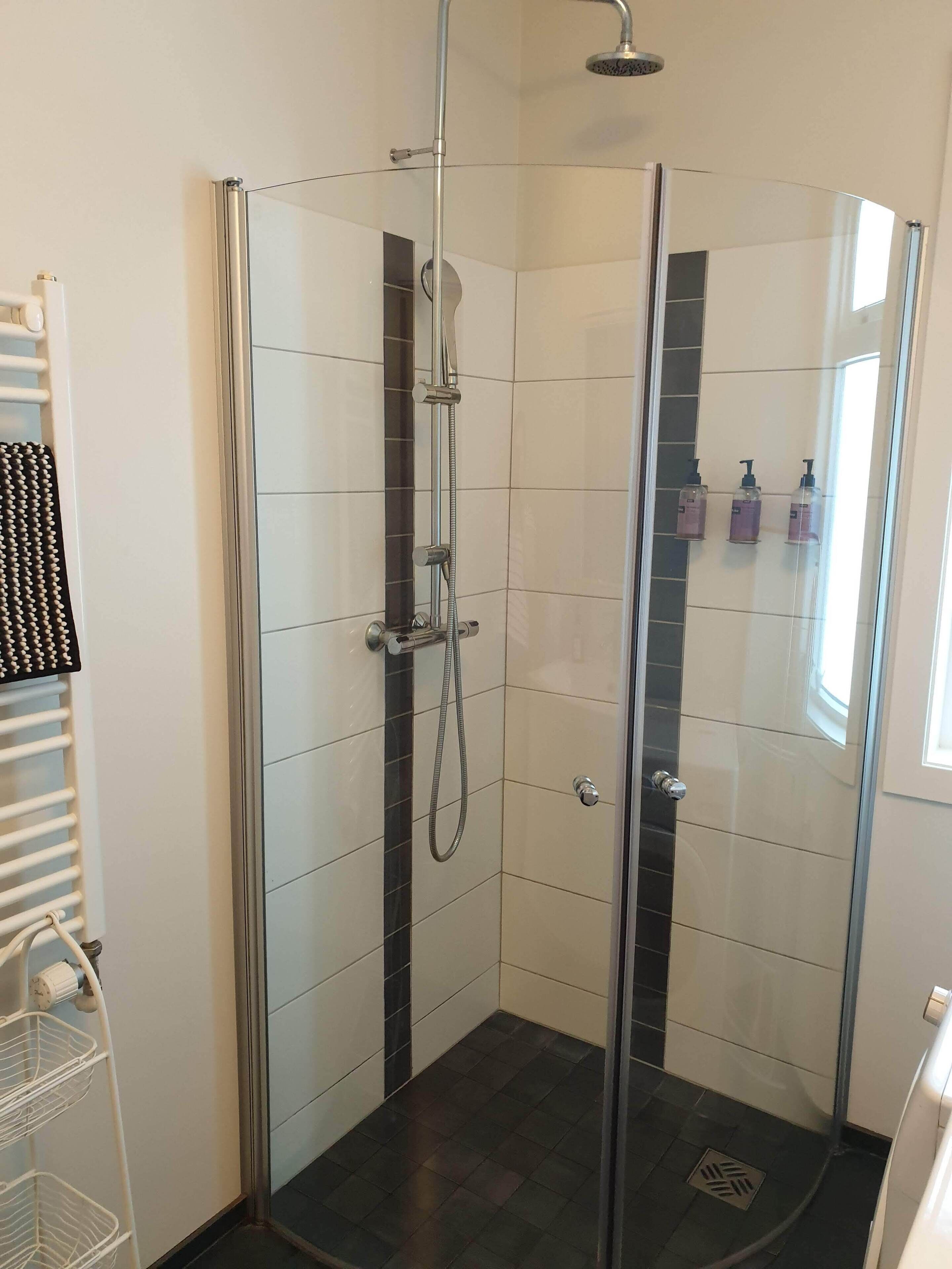 A glass-enclosed shower with a handheld showerhead and a wall-mounted faucet.