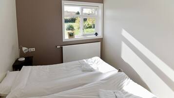 Una camera da letto con due letti, una finestra vista sul verde, una lampada da comodino e un termosifone.