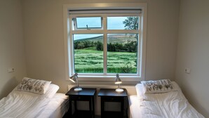 A bedroom with two beds, a window with a view of a green field, and two bedside tables with lamps. - Breidamyri Farm Apartments (Laugar)