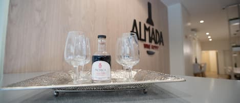 Un plateau avec une bouteille de porto tawny de la marque Pacheca et deux verres à vin vides est posé sur une table devant un mur orné du logo « ALMA DA WINE SHOP ».