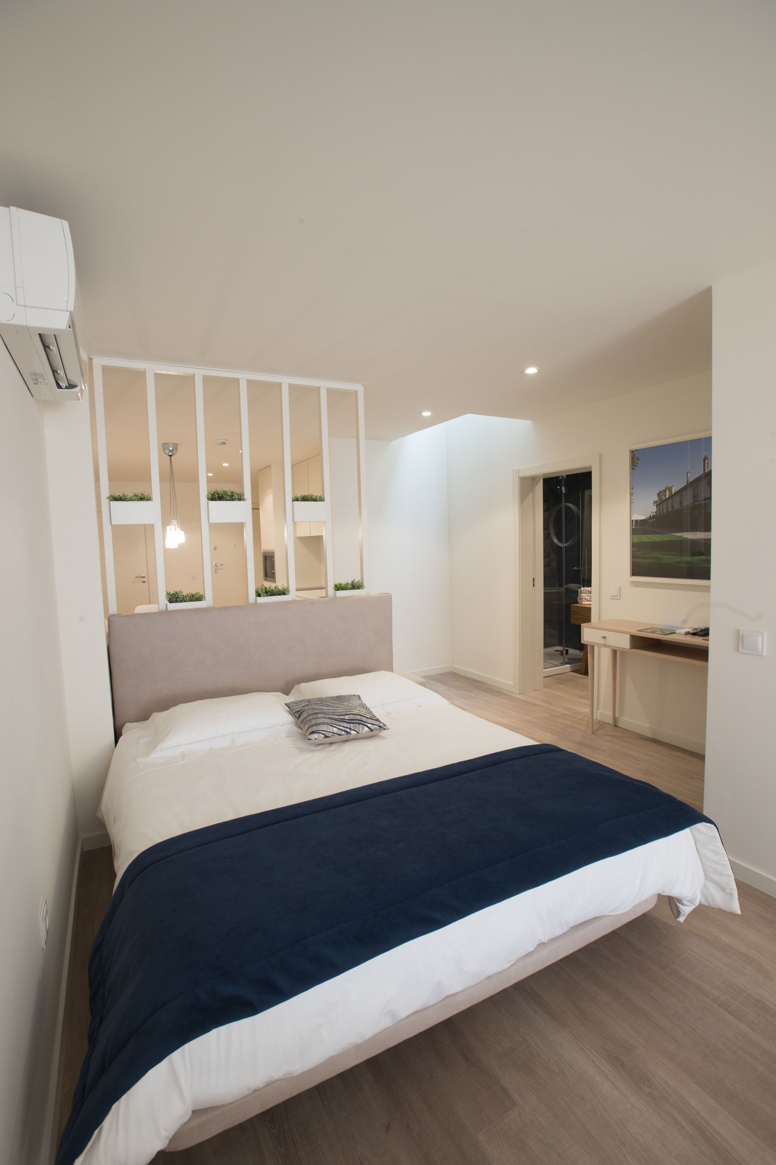 A modern bedroom with a large bed, a desk, and a mirror.
