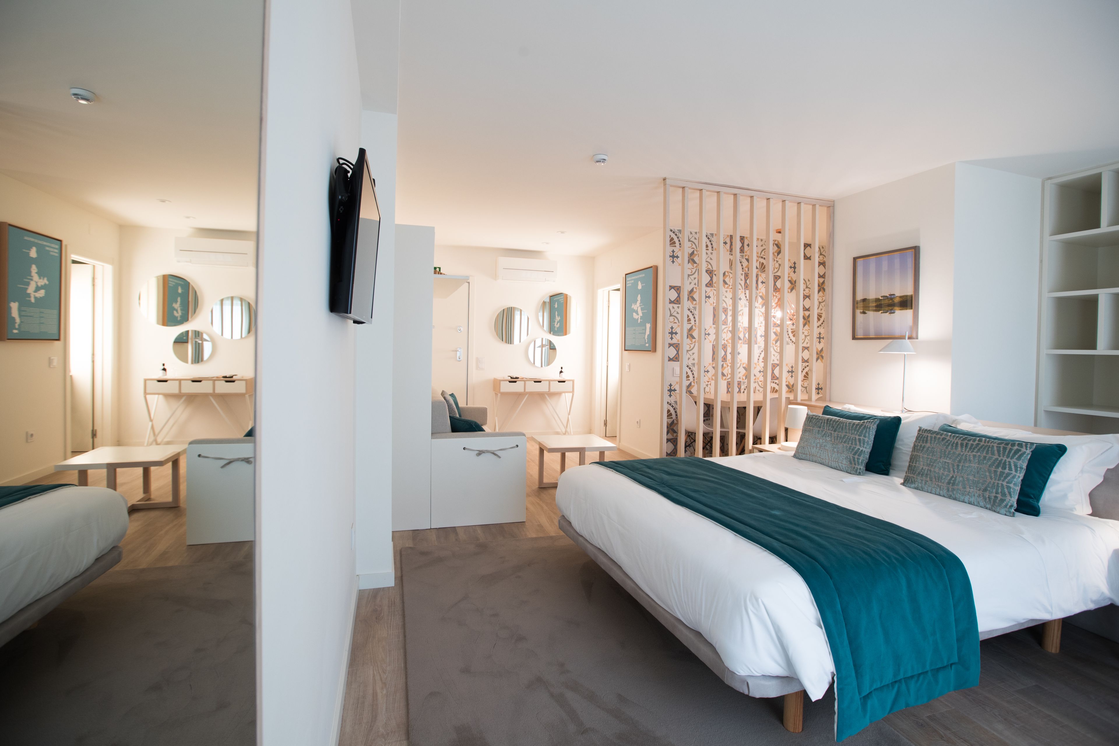 Et moderne hotelværelse med en stor seng, et skrivebord og en stol. Der er flere spejle på væggene og en dekorativ rumdeler.