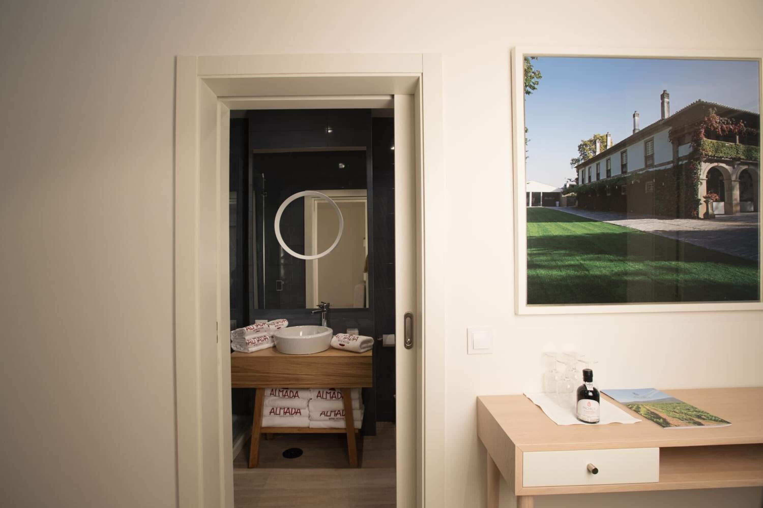 A bathroom with a wooden vanity, a round mirror, and a framed picture of a building on the wall.