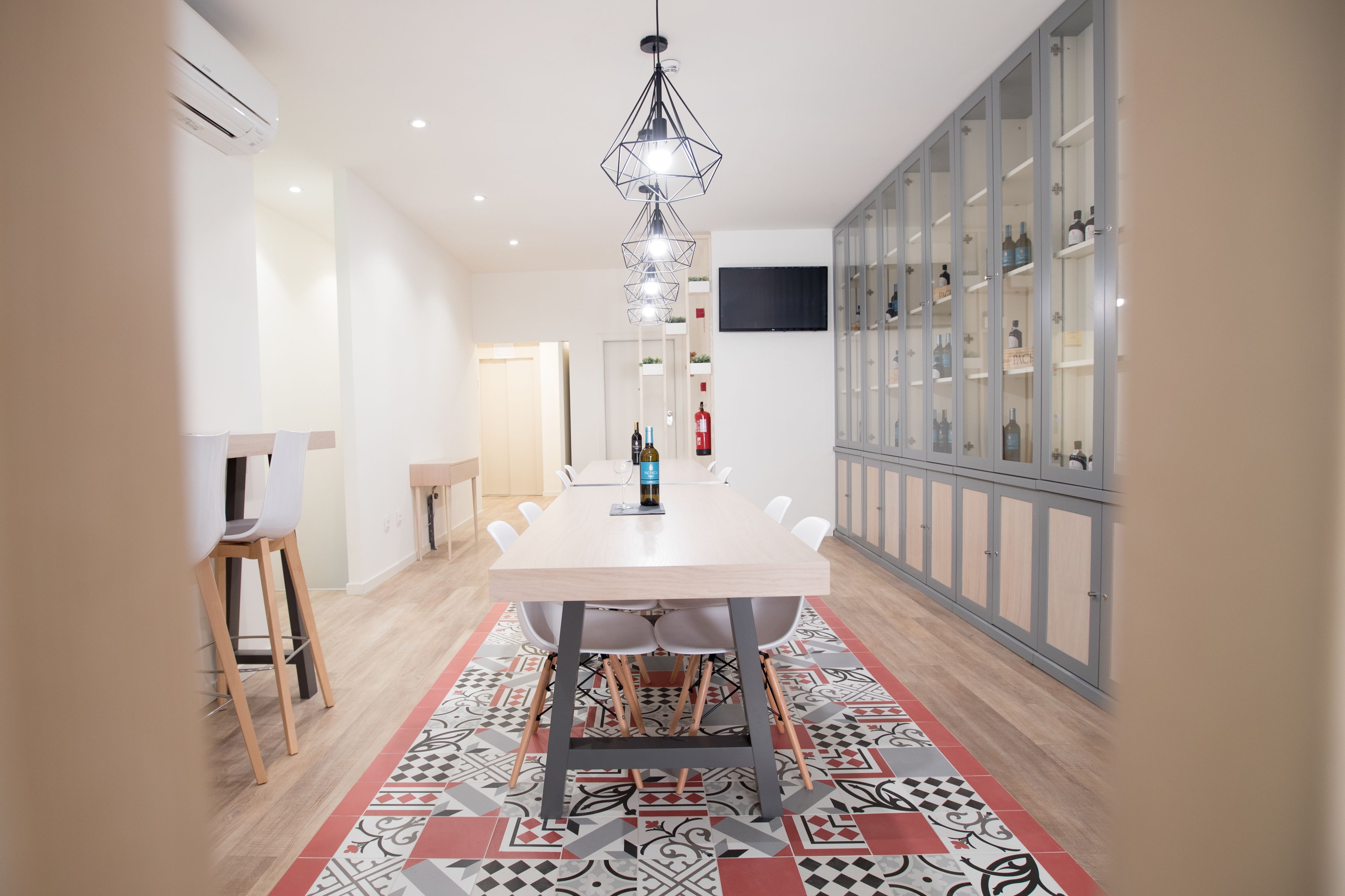 Un comedor moderno con una mesa larga, sillas, un tapete estampado, una lámpara de araña y un aparador para vinos.