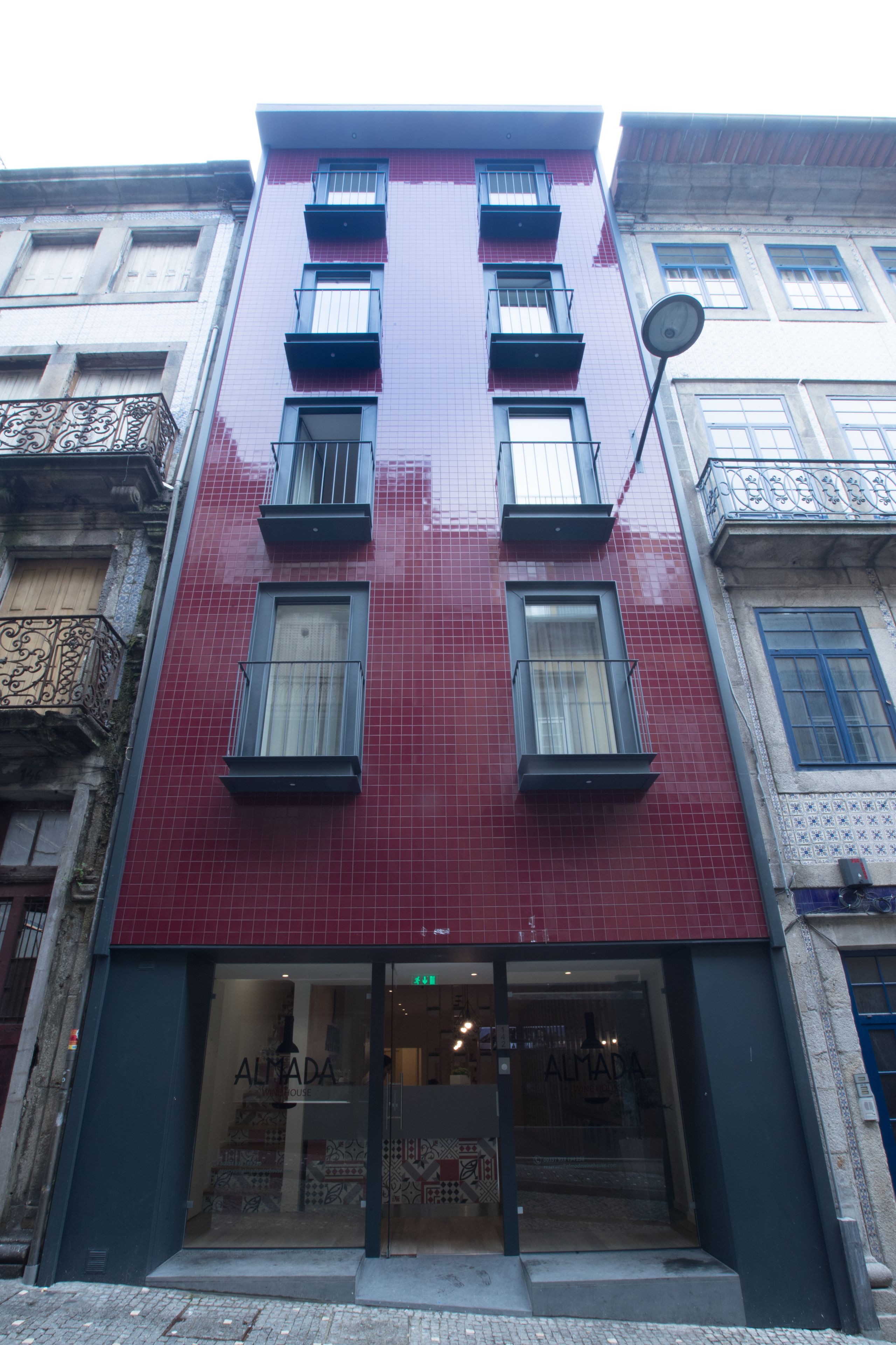 Un edificio con fachada roja, varias ventanas y un escaparate con el nombre 'ALMADA'.