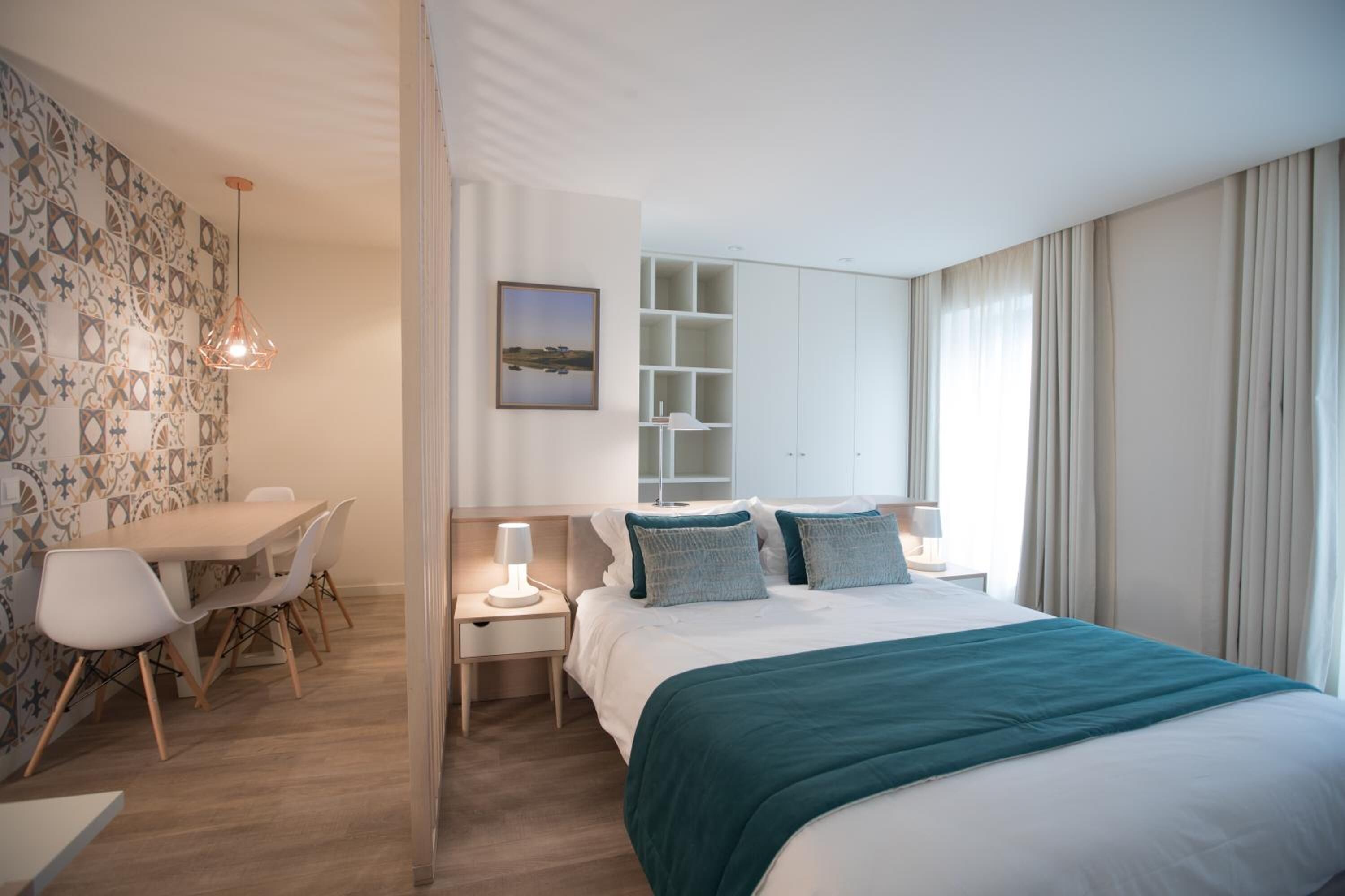Et moderne hotelværelse med en seng, sengeborde, et skrivebord og en stol. Væggen har et mønster, og der er et vindue med gardiner.