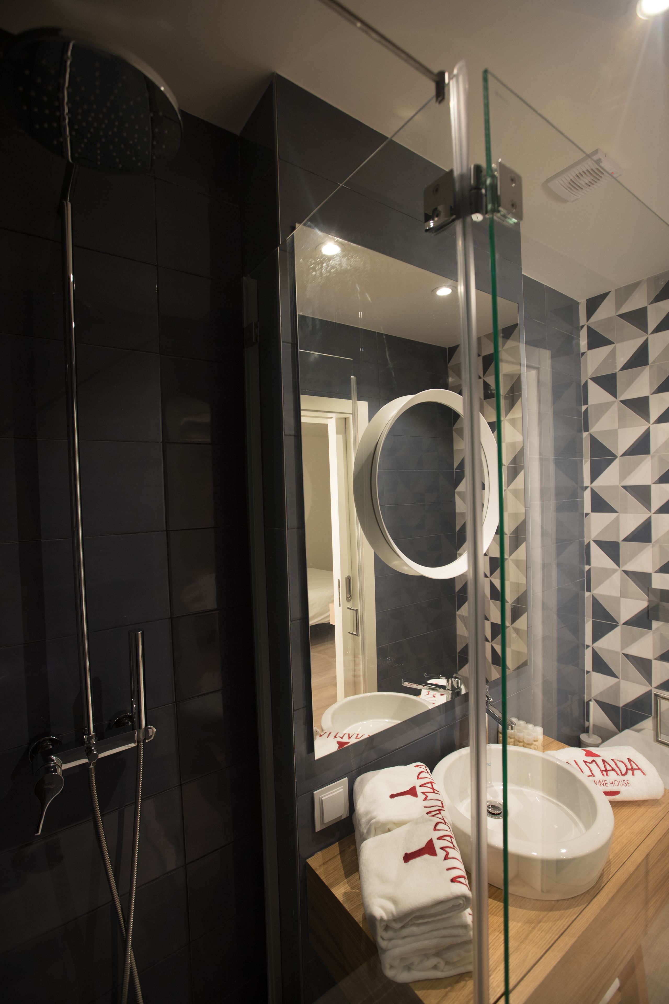 A modern bathroom with a glass-enclosed shower, a round mirror, and a sink with a towel rack.