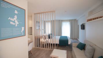 Habitació d'hotel moderna amb un llit, una taula de treball, una cadira, un sofà i una taula petita. Hi ha un mapa a la paret i un televisor a la paret.