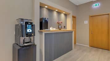 Una mesa de recepción con una máquina de café, un jarrón con flores y una puerta de madera.