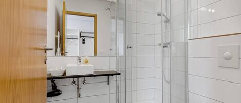 A modern bathroom with a glass shower enclosure, a toilet, a sink with a mirror, and a shelf with toiletries.