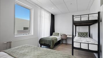 Ein Zimmer mit einem Etagenbett, einem Schreibtisch, einem Stuhl, einem Fenster mit Vorhängen und einem Heizkörper.