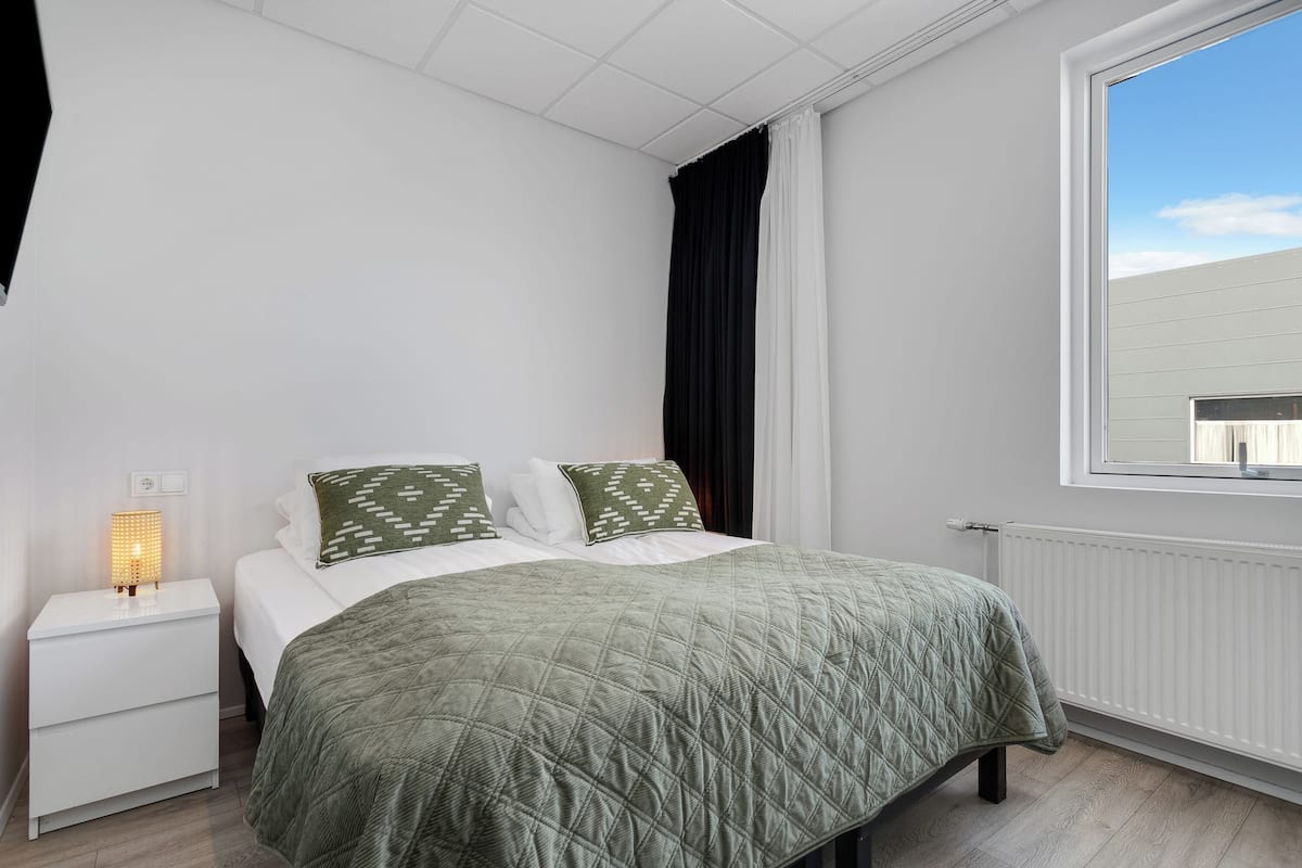 A bedroom with a bed, bedside table, lamp, and window.