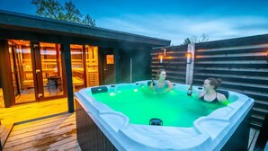 Jacuzzi con dos personas, rodeado por una terraza de madera y puertas de vidrio.